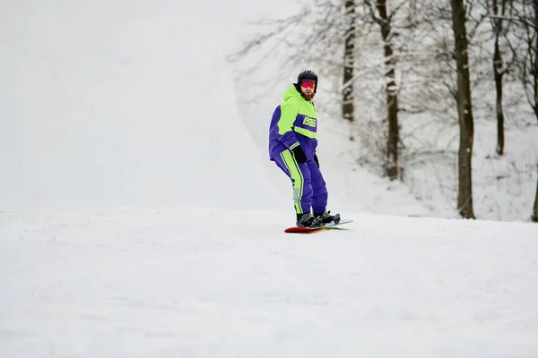 Ein bärtiger Mann gleitet sanft einen schneebedeckten Hang unter wolkenverhangenem Himmel hinunter und hat Spaß beim Snowboarden. — Stockfoto