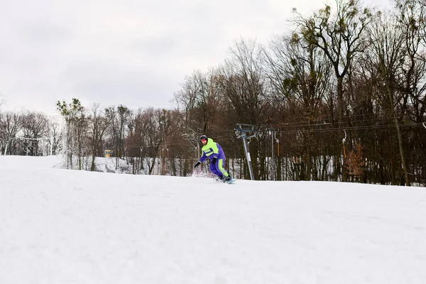 Un homme barbu monte son snowboard sur une pente enneigée entourée d'arbres. — Photo de stock