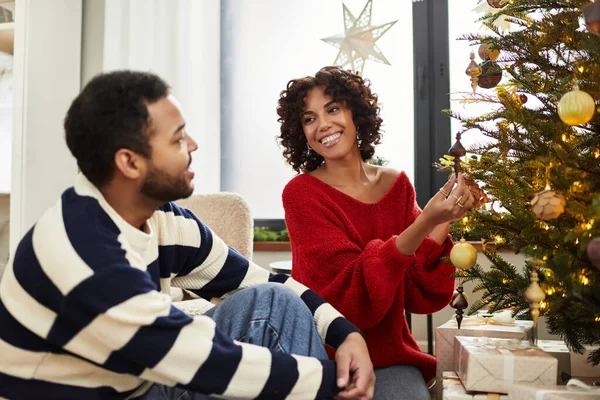 Fröhliches afroamerikanisches Paar genießt gemeinsame Zeit beim Schmücken eines festlichen Weihnachtsbaums im Haus. — Stockfoto