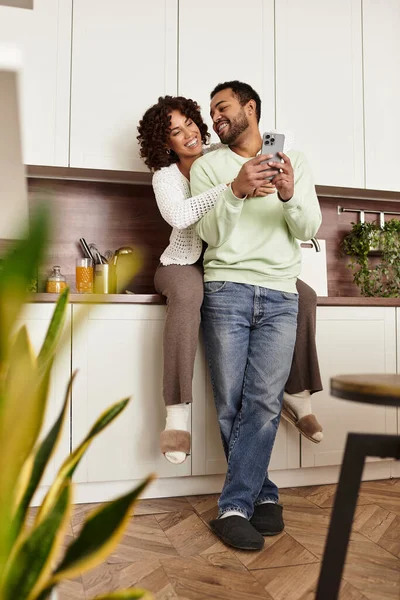 Ein glückliches afroamerikanisches Paar entspannt sich zu Hause, lächelt und lacht beim Telefonieren. — Stockfoto