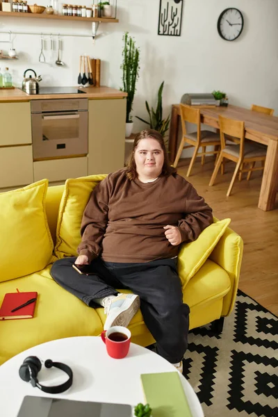 A young woman with Down syndrome relaxes on a yellow couch in a cheerful living room. — Stock Photo