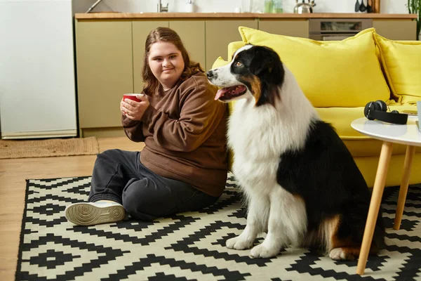 A young woman with Down syndrome relaxes at home, sipping coffee beside her loyal dog. — Stock Photo