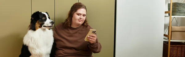 En un espacio acogedor, una joven con síndrome de Down se sienta junto a su perro, enfocada en su teléfono. - foto de stock