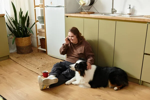 A young woman with Down syndrome chats happily on the kitchen floor beside her dog. — Stock Photo