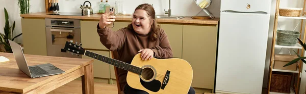 Felice giovane donna con sindrome di Down suona la chitarra e si connette con gli amici online nella sua cucina. — Foto stock