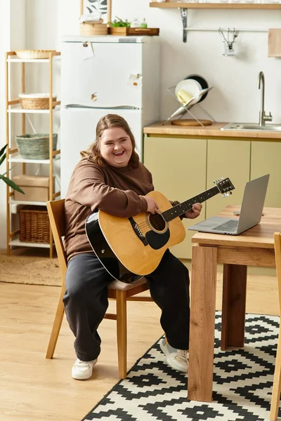 A young woman with Down syndrome smiles while strumming her guitar in a warm, inviting kitchen. — Stock Photo