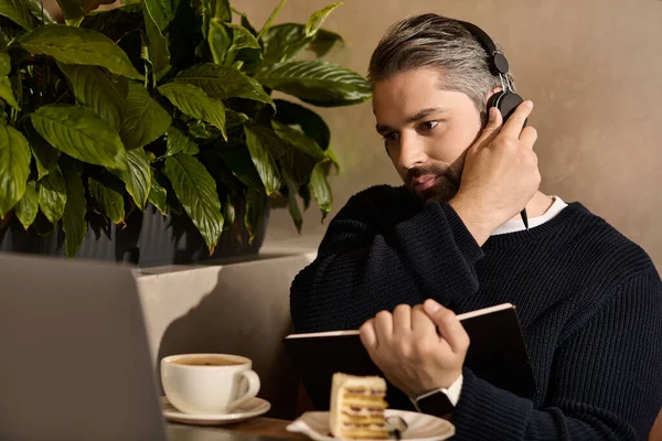 Stylish man with headphones deeply engaged in work, savoring coffee and dessert in a cafe. - foto de stock