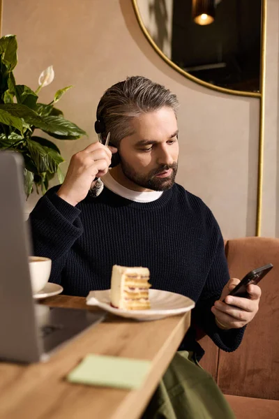A handsome, mature man sits at a cozy cafe, enjoying cake and talking on the phone. — Stockfoto
