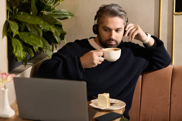 Красивый мужчина расслабляется с чашкой кофе, сосредоточенный на своем ноутбуке в элегантном кафе. — стоковое фото