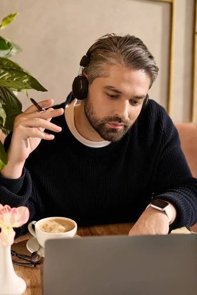 Mature man in stylish attire is focused on his work while sipping coffee and listening to music. — Stockfoto