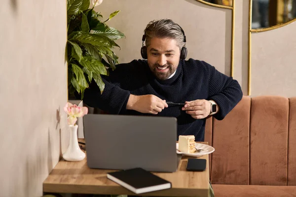 Handsome man in stylish attire smiles while video chatting at a tranquil cafe with dessert. — Stockfoto