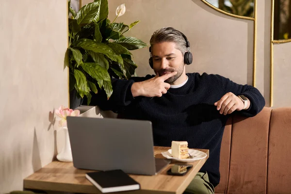 A mature man in stylish attire smiles as he enjoys dessert while focusing on his laptop. — Stockfoto