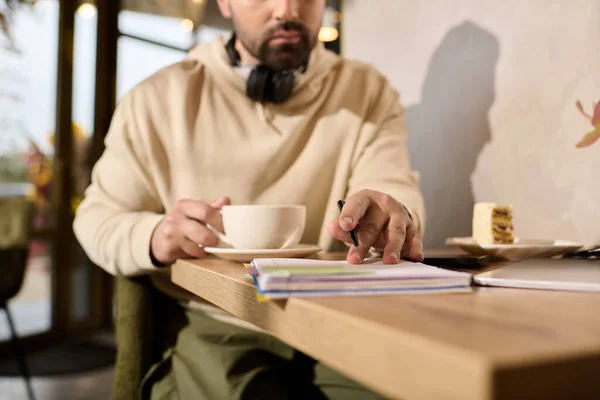Handsome man in trendy attire sips coffee while contemplating at a cozy cafe table. — Stockfoto
