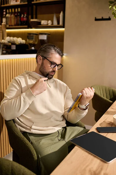 Handsome gentleman dressed in fashionable attire reads while seated comfortably in a cozy cafe. — Stockfoto
