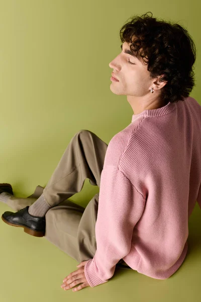 Um homem bonito em um suéter rosa e calças marrom senta-se graciosamente, exalando senso de moda e charme. — Fotografia de Stock