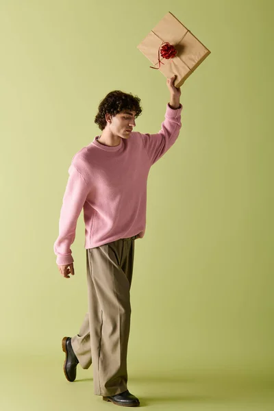 Уверенный в себе человек в стильной одежде ходит с гордостью, держа завернутый подарок в воздухе. — стоковое фото