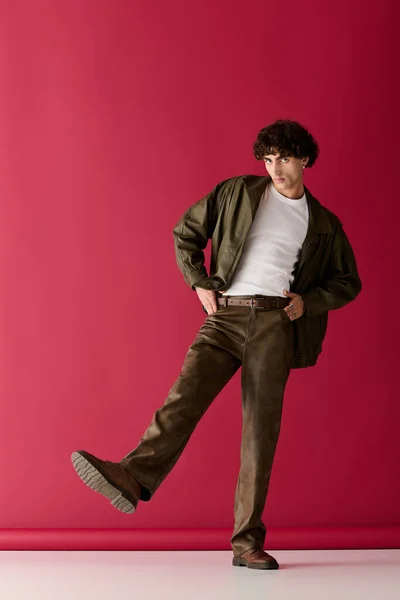 Красивий чоловік у стильному вбранні впевнено позує перед вражаючим червоним тлом. — стокове фото