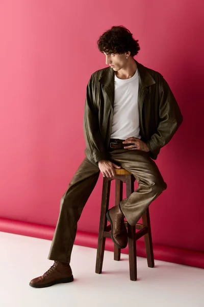 Un hombre guapo elegantemente vestido en un conjunto elegante se sienta en un taburete, destacando su sentido de la moda. - foto de stock