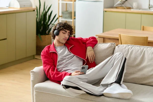 Ein junger Mann hört Musik über Kopfhörer und lümmelt auf einem gemütlichen Sofa in einem modernen Haus. — Stockfoto