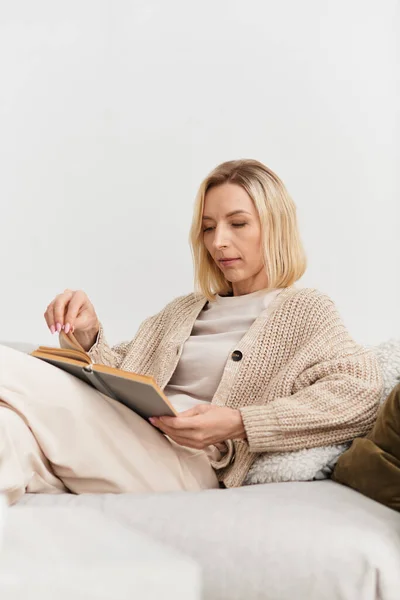 Блондинка відпочиває вдома, читаючи книгу, одягнену в м'який і затишний одяг. — стокове фото