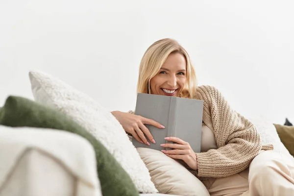 Блондинка насолоджується спокійним днем вдома, загорнута в кардиган під час читання. — стокове фото