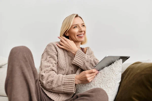 Eine blonde Frau entspannt auf der Couch in ihrer stilvollen Wohnung und genießt die Freizeit mit einem Tablet. — Stockfoto
