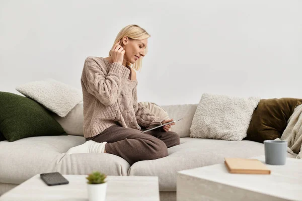 Una mujer rubia en ropa acogedora se relaja en el sofá, disfrutando de una tarde tranquila. - foto de stock