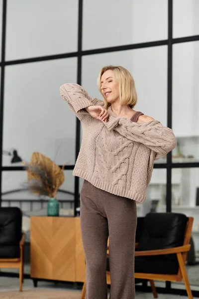 Mujer rubia relajada disfrutando de un momento acogedor en casa, vistiendo ropa suave en la dicha de invierno. - foto de stock