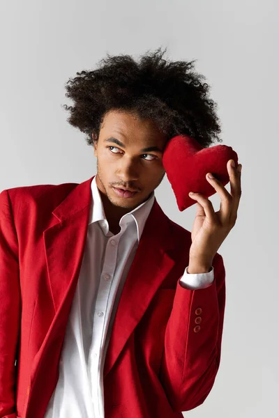 A handsome young man dressed in elegant attire holds a red heart cushion, expressing joy and style. — Stockfoto