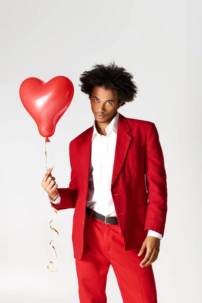 A stylish young man in a red suit holds a heart shaped balloon, exuding charm and confidence. — Stockfoto