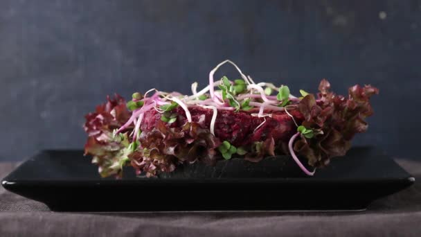 Homemade vegan black burger with beetroot cutlet, sprouts, champignon and green salad on black plate over dark background — Stock Video