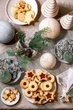 Ev yapımı geleneksel Noel Linz kurabiyeleri ve kırmızı reçelli kurabiyeler. Keten masa örtüsü üzerine ahşap çevre dostu xmas dekorasyonları. Tatil masası ayarı.