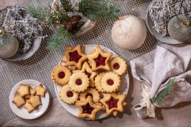 Ev yapımı geleneksel Noel Linz kurabiyeleri ve kırmızı reçelli kurabiyeler. Keten masa örtüsü üzerine ahşap çevre dostu xmas dekorasyonları. Tatil masası ayarı.