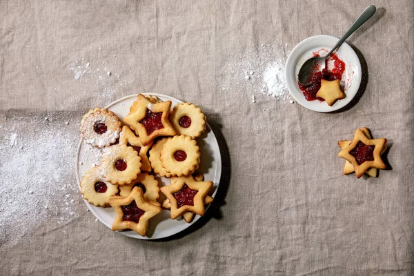 自家製の伝統的なリンツのショートブレッドビスケットクッキーで 赤いジャムとアイシングシュガーがリネンのテーブルクロスの上にセラミックプレートに乗っています — ストック写真