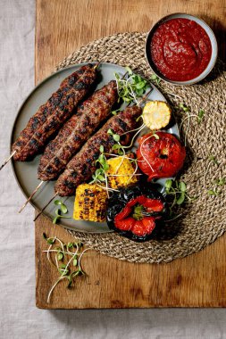 Doğu fast food. Tabakta ızgara baharatlı biftek, liulya kebabı ızgara sebze, mısır koçanı, domates ve kırmızı biber, ahşap masada domates sosu. Düz yatıyordu