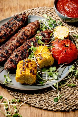 Doğu fast food. Baharatlı ızgara biftek, liulya kebabı. Düz ekmek, ızgara sebze, mısır koçanı, domates ve kırmızı biber, ahşap masada domates sosu..