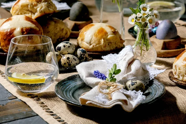 复活节餐桌摆设 有彩蛋和巧克力蛋 热十字面包 餐巾纸的空陶瓷盘 木制餐桌上的一杯柠檬水和纺织品桌布 — 图库照片