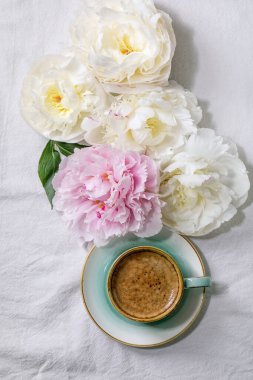 Bir fincan espresso kahve, pembe ve beyaz şakayık çiçekleri beyaz pamuk tekstil arka planında yapraklar. Düz yat, boşluğu kopyala