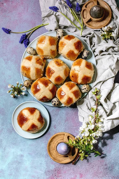自家製イースター伝統的なホットクロスパンは ムスカリの花 花の枝 ウズラの卵 青いテクスチャの背景に織物とセラミックプレート上に — ストック写真