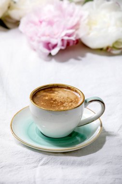 Bir fincan espresso kahve, pembe ve beyaz şakayık çiçekleri beyaz pamuk tekstil arka planında yapraklar. Düz yat, boşluğu kopyala