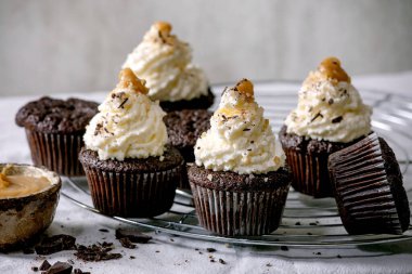 Beyaz krem şantili ve tuzlu karamelli ev yapımı çikolatalı kekler, beyaz masa örtüsü üzerinde doğranmış siyah çikolatalı kekler..