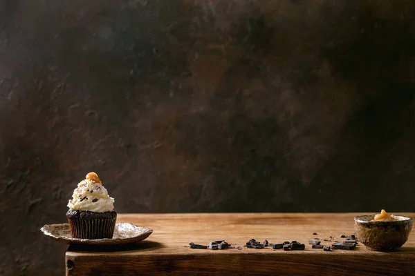 自制巧克力杯蛋糕松饼与白色奶油奶油和盐渍焦糖陶瓷盘 与切碎的黑巧克力在木制桌子上 复制空间 — 图库照片