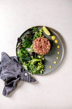 Ton balıklı tartar, yeşil salata, limon, avokado ve hardal sosu beyaz dokuya seramik tabakta servis ediliyor. Düz konum, kopyalama alanı. Güzel yemekler, restoran aperatifleri.