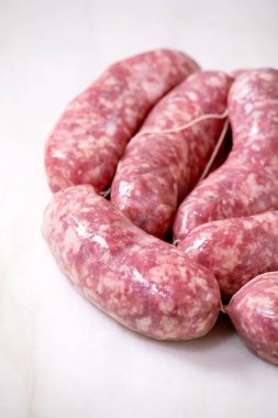 Beyaz mermer arka planda bir tabak çiğ İtalyan sosisi salsiccia. Yeşil salata, sebze ve domates sosu. Kapat.