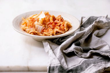 Beyaz mermer masanın üzerinde seramik tabakta servis edilen ev yapımı Kore geleneksel mayalanmış kimchi lahanası..