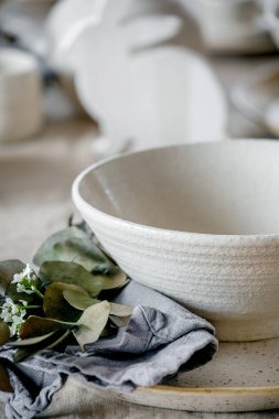 Boş seramik masa takımları, tabaklar ve kaselerle dolu kırsal Paskalya sofrası, Paskalya tavşanı süslemeleri, pencerenin önündeki keten masa örtüsünde vazo dalları. Paskalya bayramı yemeği.