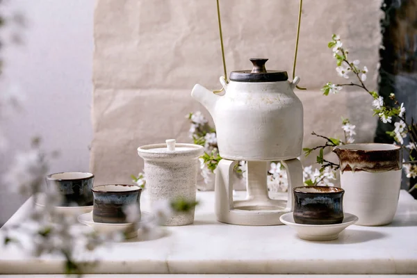 白色和黑色工艺手工制作的陶瓷茶壶 配有黑色陶瓷杯 山口壶和盛开的樱桃树作为装饰矗立在大理石桌上 传统的日本茶道 Teadrinking — 图库照片