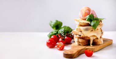 Kızarmış peynirli sandviç, jambonlu sandviç, kiraz domatesli ve fesleğen yapraklı beyaz mermer masadaki tahta kesme tahtası. Sancak boyutu