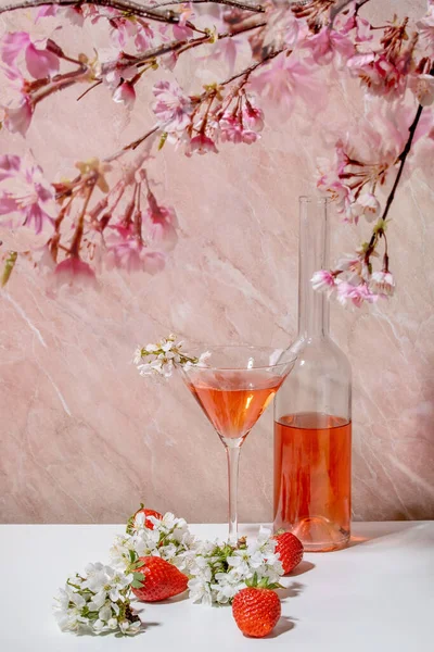マルティーニグラスでストロベリーアルコールやノンアルコールカクテルをコンセプトに 白やピンクの大理石を背景に桜の枝を飾ったグラスボトル — ストック写真