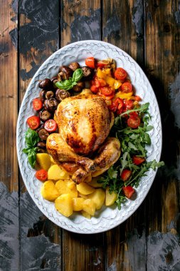 Izgara ızgara tavuk, sebze garnitürlü dolmalık biber, soğan, fırında patates, kiraz domatesleri, mantarlar ve koyu ahşap zemin üzerine seramik tabakta otlar. Üst manzara, düz uzanma